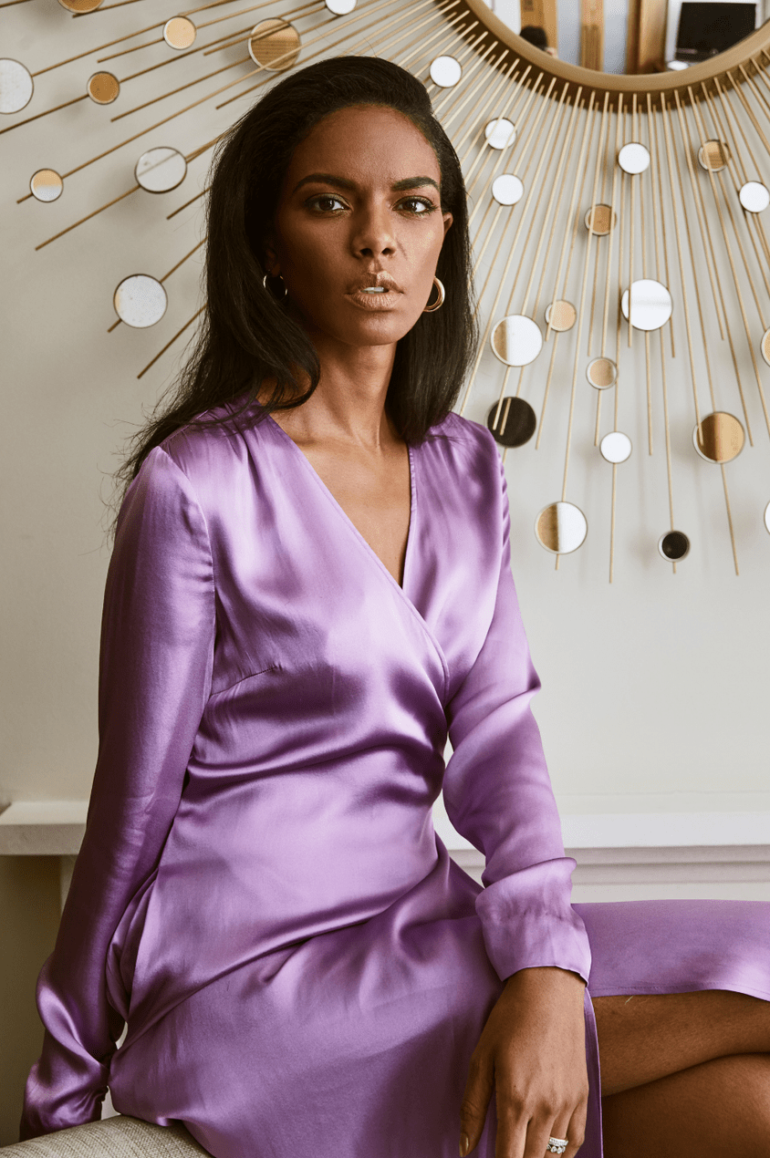 Noëlla Coursaris Musunka wears a purple satin wrap dress with gold hoops
